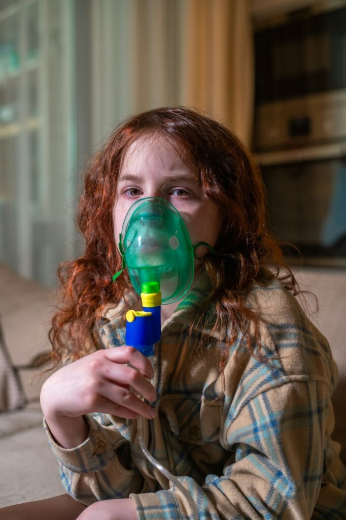 Sick girl making inhalation with nebulizer to reduce coughing, at home, child taking medication
