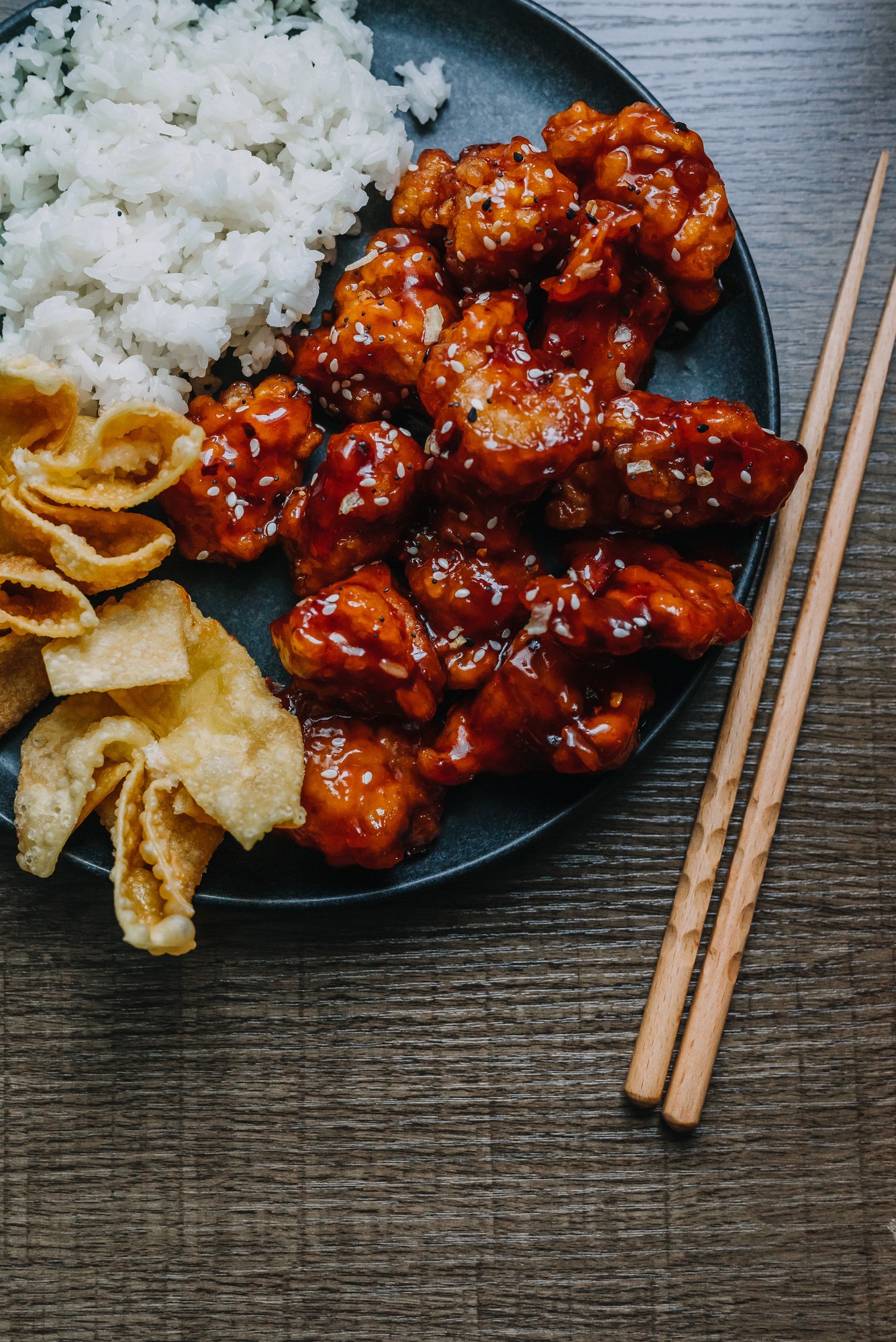 General tsos chicken with white rice and crab rangoon on a dark dish