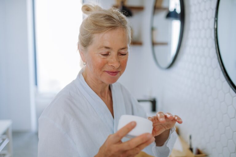 Beautiful senior woman in bathrobe applying natural cream in bathroom, skin care and morning routine