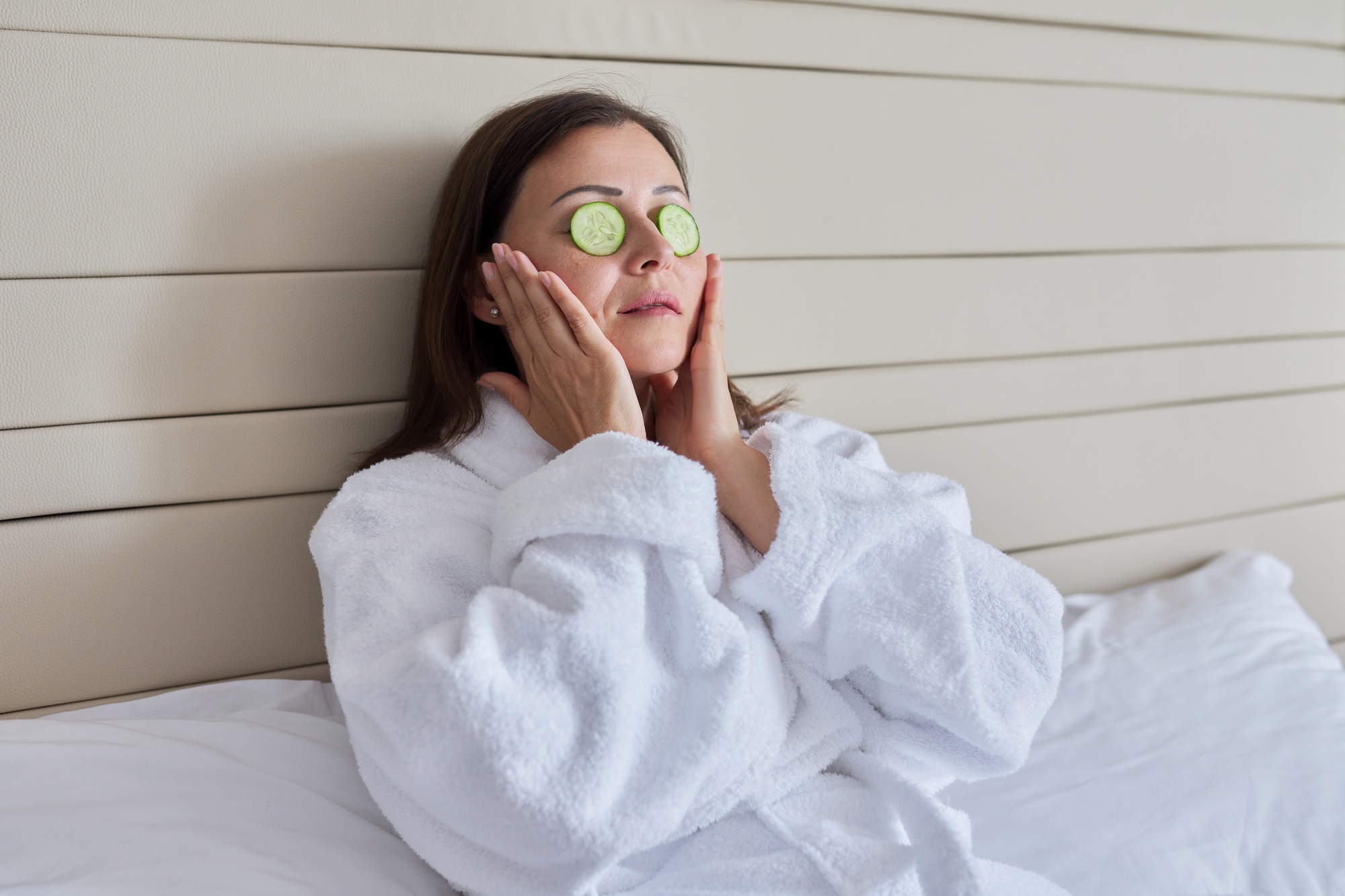 Mature female in bathrobe doing home spa treatments with cucumbers
