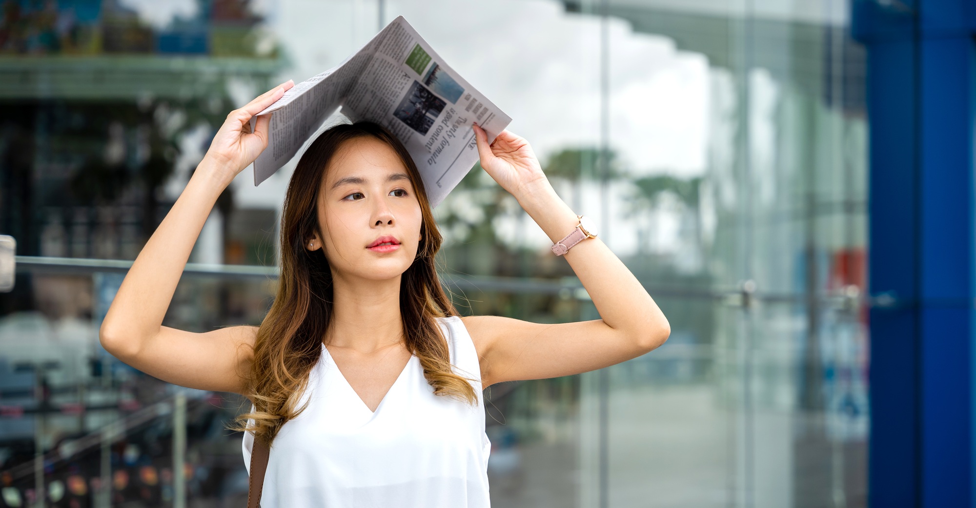 Overwhelmed by city living, an Asian woman covers her face with a newspaper